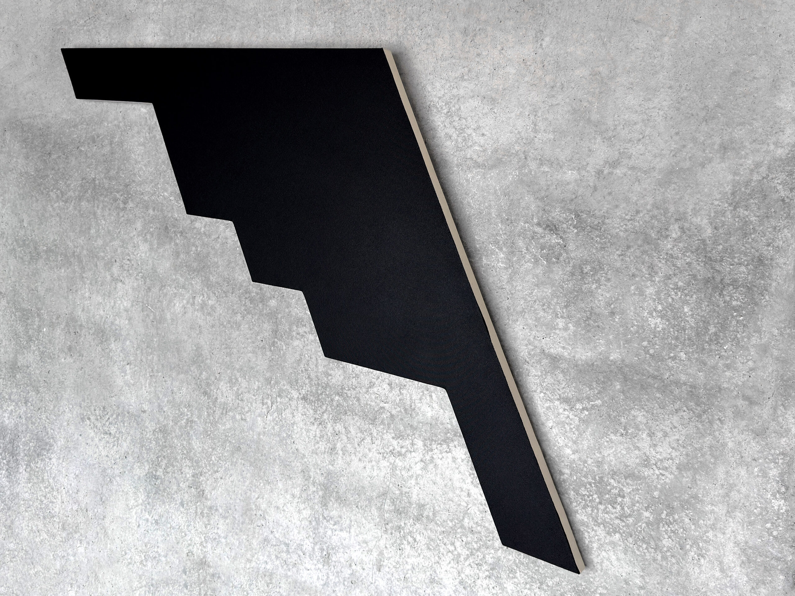 Side perspective view of Jean-Charles Kien's black geometric shaped canvas artwork on a gray concrete wall